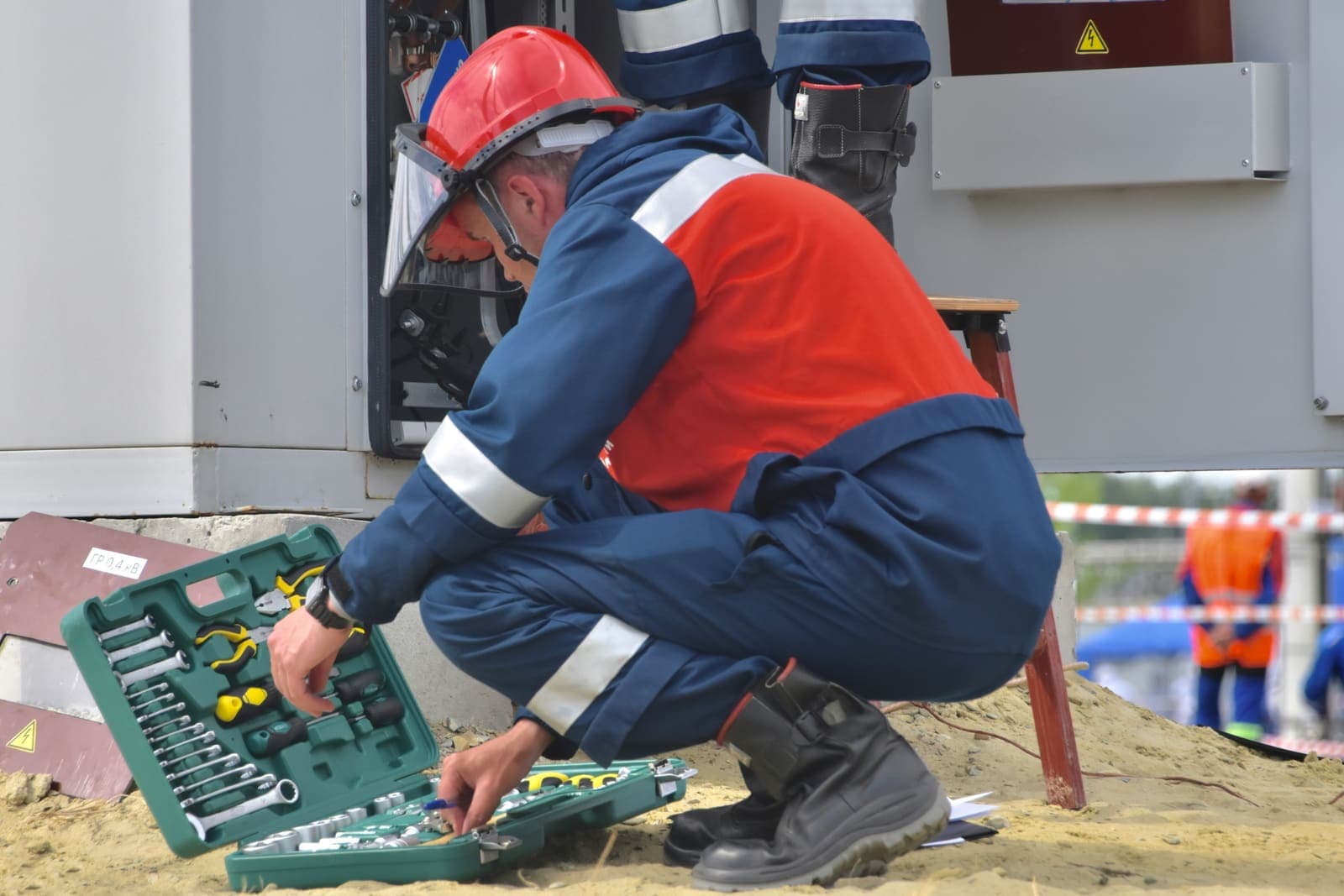 Electricista en cuclillas trabajando sobre un tablero, con su caja de herramientas abierta